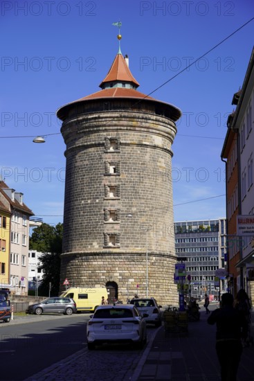 Massive round tower made of bricks, surrounded by city buildings under a clear sky, Nuremberg,