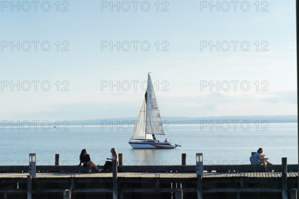 Lake Neusiedl, Burgenland, Austria, Europe, A sailboat sails calmly on a lake while people relax on