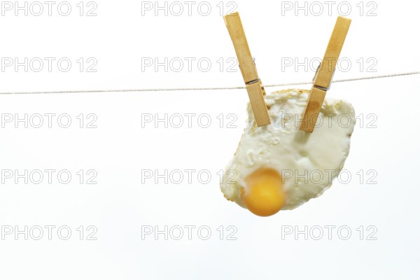 Clothespins holding fried egg on clothesline against white background, creating a quirky and