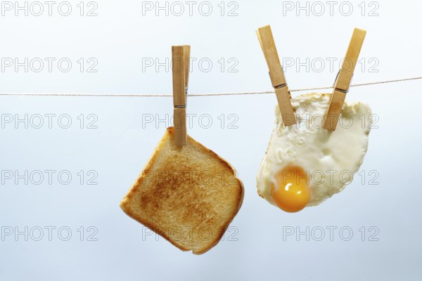 Toasted bread and fried egg are hanging from a clothesline with wooden clothespins, representing a