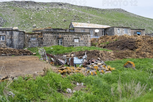 Stone house in a rural area surrounded by green hills and rocks, cow dung in front, Ardenis, Shirak