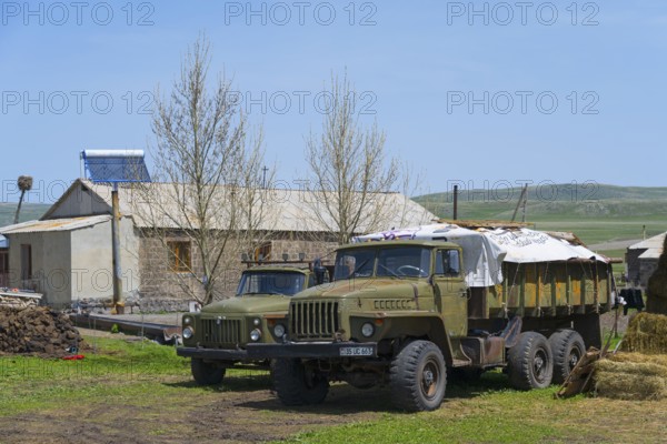Large lorries parked on a farm in front of a stone building surrounded by green countryside, Gaz 53