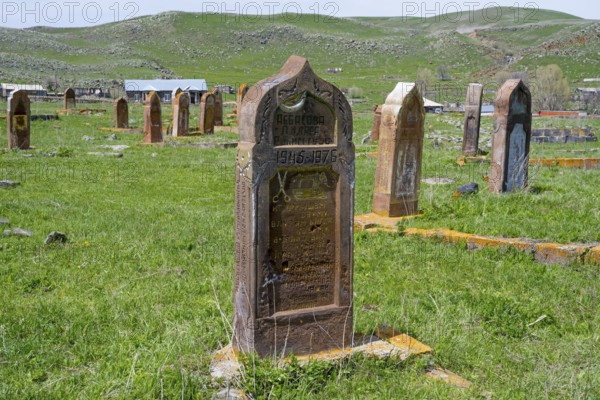 A well-preserved old gravestone on green grass in front of a hilly landscape with several