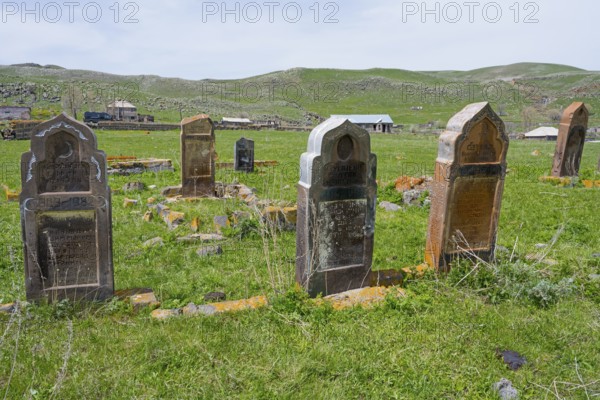 Cemetery with old weathered gravestones on green grassland with rolling hills in the background,
