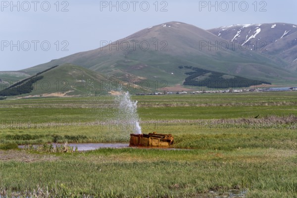 A tranquil landscape with hills and a water fountain in a green meadow, geyser near Karmravan,