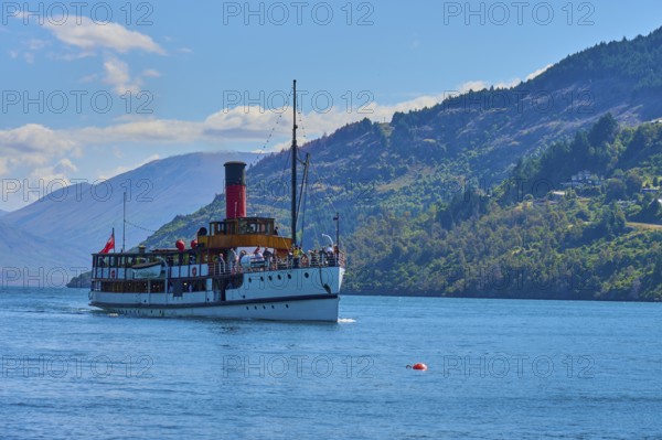 Large ship sailing across a wide lake with picturesque mountain ranges in the background,