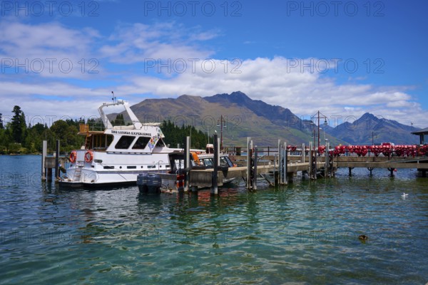 Boat at a jetty on a tranquil lake with surrounding mountain scenery, Queenstown, Queenstown-Lakes