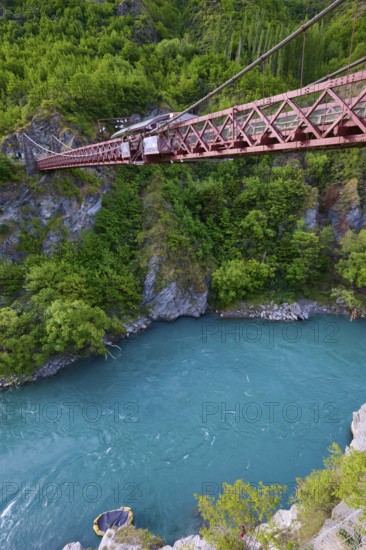 Red suspension bridge over river with steep wooded cliffs and calm waters, Kawarau Gorge Suspension