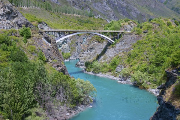 A bridge spans a turquoise-coloured river in a green and rocky landscape, Kawarau River,