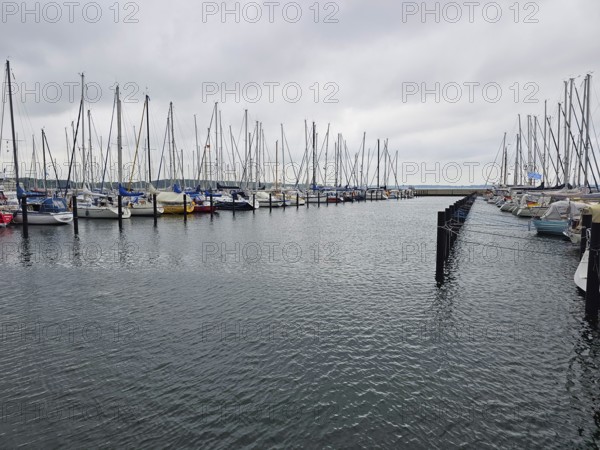 Numerous moored sailing boats in the harbour with cloudy sky, calm sea and parallel jetties, Laboe,