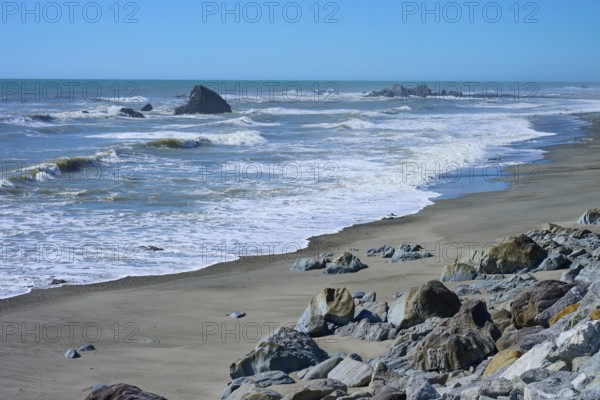 The waves gently lap against a wide sandy beach with scattered rocks, West Coast, South Island, New