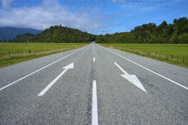 Long empty road with directional arrows through rural surroundings, West Coast, South Island, New