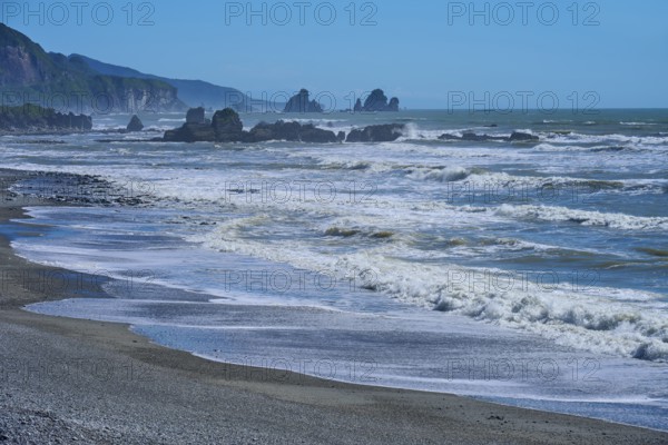 Dynamic waves roll onto a rocky beach under a bright blue sky, West Coast, South Island, New