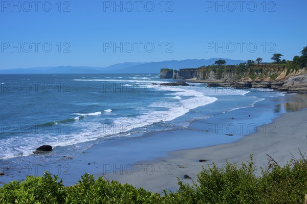 A peaceful coastal landscape with blue waves crashing against sand and cliffs under a clear blue