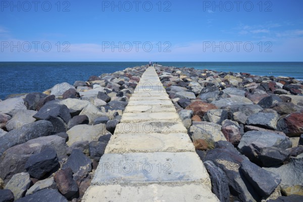 A stony path leads into the sea, surrounded by a sunny coastal landscape, Mana Bay, Patea,