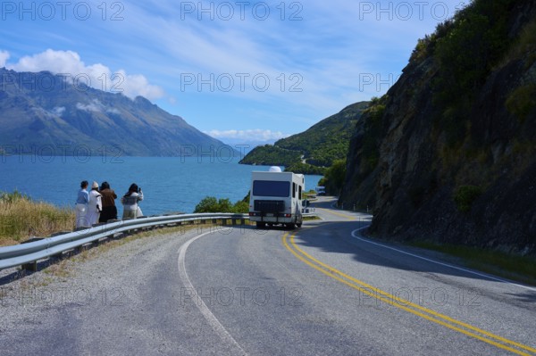 People enjoying travelling and a motorhome on a winding road next to a lake surrounded by