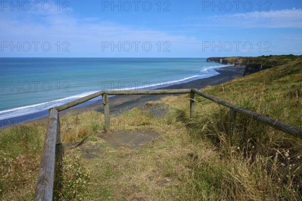 Viewing platform with wooden railing overlooks black sand beach and cliffs on a quiet coast, Mana