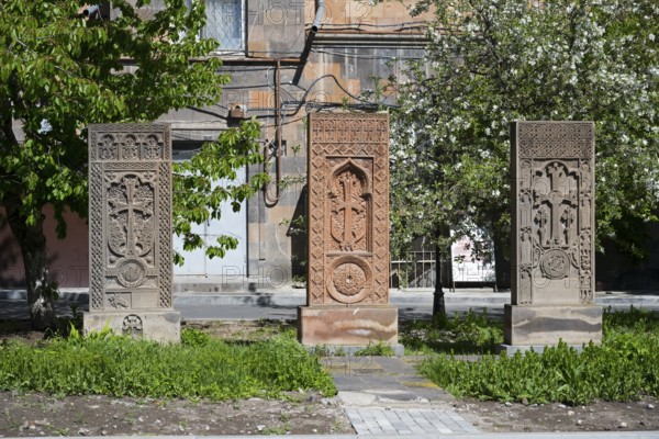 Three artistically engraved khachkars stand in a green setting, cross stones, khachkars, Gyumri,