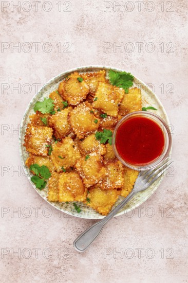 Fried ravioli with parmesan cheese, served with red sauce and garnished with herbs, on a light