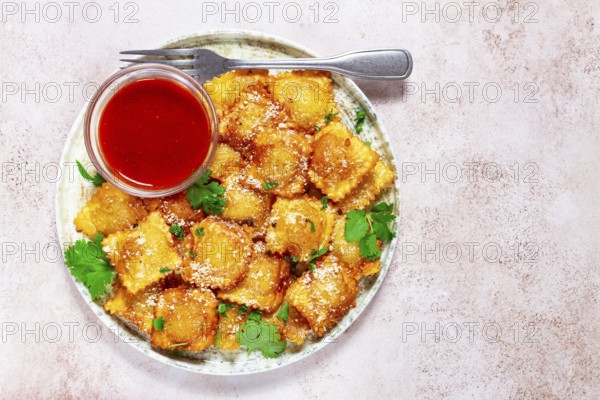 Fried ravioli with parmesan cheese, served with red sauce and garnished with herbs, on a light