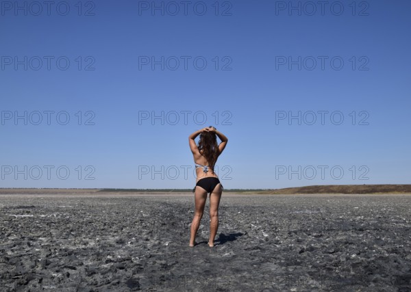 Walk the dark-haired woman in a swimsuit on the bottom of a dry lake with salt and mud. Taman,
