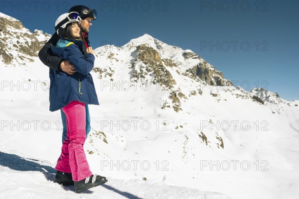 Young caucasian couple pose hug enjoying looking at snowy mountains range in winter. Get away