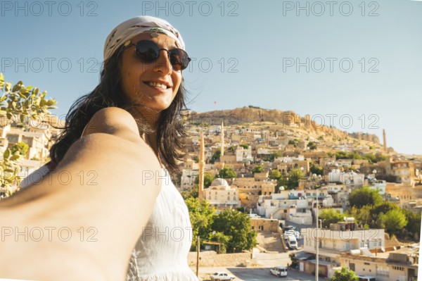 Smiling woman in sunglasses taking selfie with panoramic skyline of historic Mardin Turkey and