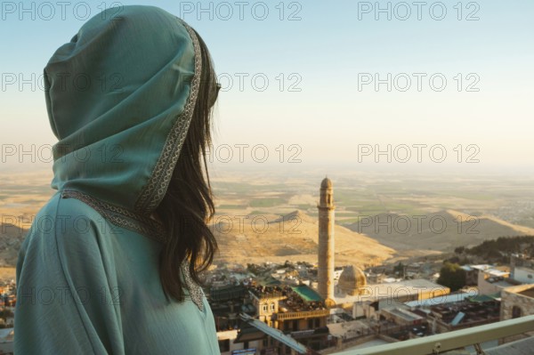 Smiling woman traveler in abaya standing above Mardin Turkey with panoramic view of Mesopotamian