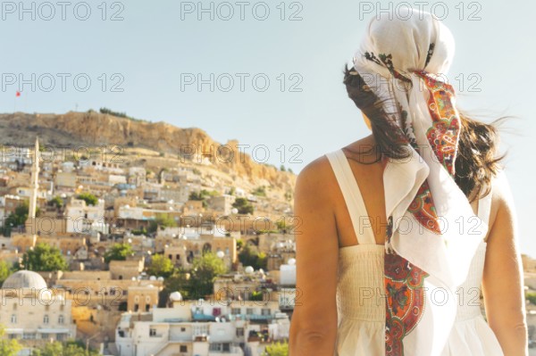 Traveler woman in white dress looking over panoramic view of historic city of Mardin Turkey with