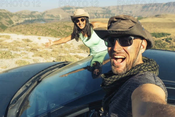 Happy young caucasian couple taking selfie while sitting in rented vehicle black car having road