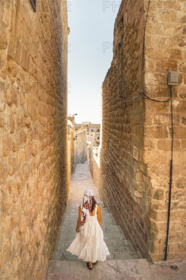Traveler woman in white dress walking through narrow stone alley in historic city of Mardin Turkey