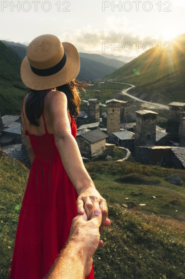 Young Couple holding hands leading way in Ushguli Georgia woman in red dress leading towards