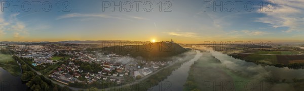 The sun rises over a city surrounded by fog. The picture shows the river landscape of the Danube