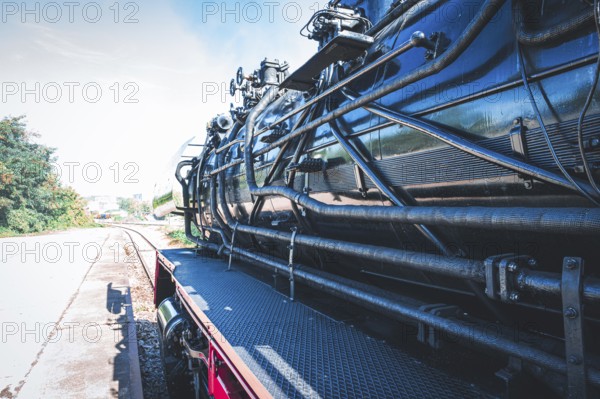 Partial view of a shiny steam locomotive showing the detailed mechanics and the railway landscape,