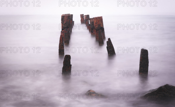 Wooden bridge remains in silky water with sea horizon in the background. Concept of time and