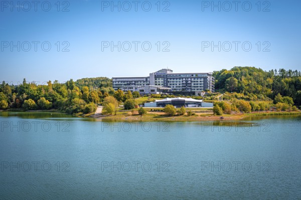 Organic lakeside hotel surrounded by trees under a clear blue sky, Zeulenrodaer Meer reservoir,