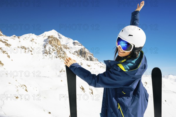 Young happy caucasian woman pose with skis looking at camera hands up in alpine zone. Get away