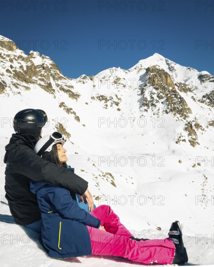 Young caucasian couple pose sits hug enjoying looking at snowy mountains in winter. Get away skiing