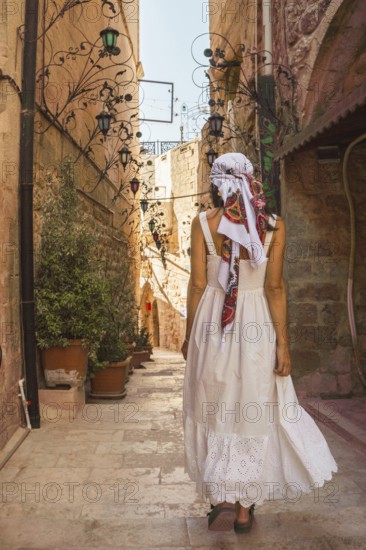 Traveler woman in white dress walking through narrow stone alley in historic city of Mardin Turkey