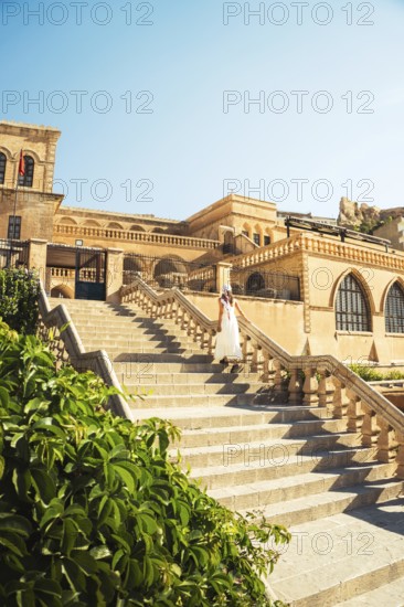 Traveler woman in white dress walking stairs of historic building - visit Mardin museum in old city