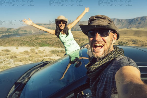 Happy travelers taking selfie photo on summer road trip with rented car in Turkey, symbolizing