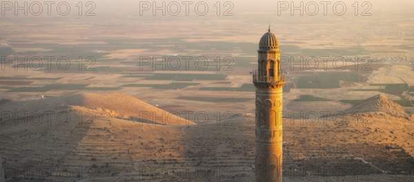 Historic Ulu Cami mosque minaret in Mardin Turkey illuminated by sunset against vast Mesopotamian