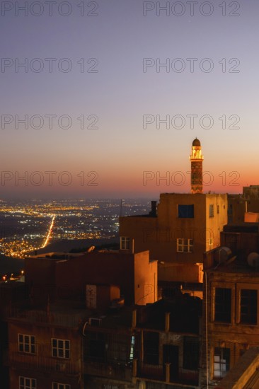 Illuminated mosque minaret above Mardin old town with glowing city lights and Mesopotamian plains