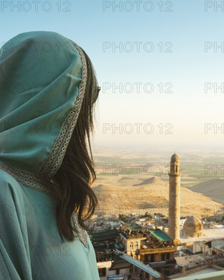 Smiling woman traveler in abaya standing above Mardin Turkey with panoramic view of Mesopotamian