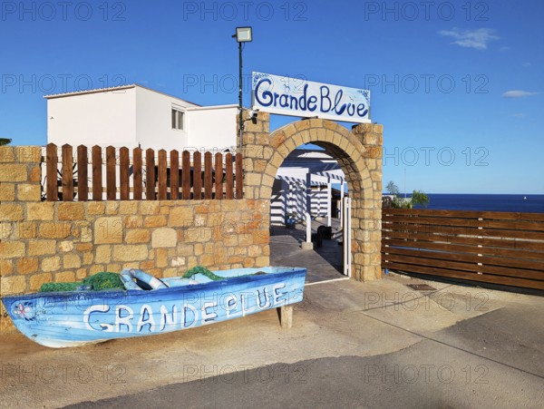 Exterior view of the Grande Blue Restaurant on the coast with a decorative boat and a stone
