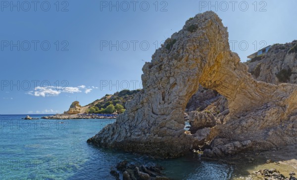 Grande Blue coast with a natural stone arch in front of clear blue water under a sunny sky, Grande