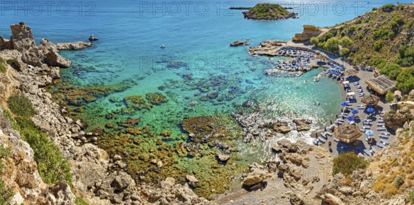 Secluded Grande Blue Bay with clear turquoise water and rocks, along which a row of beach loungers