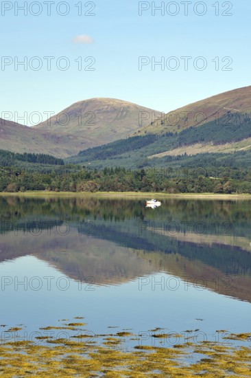 A peaceful body of water reflecting the surrounding mountains and a clear blue sky, Loch Eil,