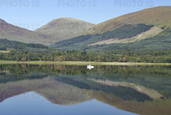 A boat on a glassy loch surrounded by mountains under a clear sky, Loch Eil, Scotland, Great