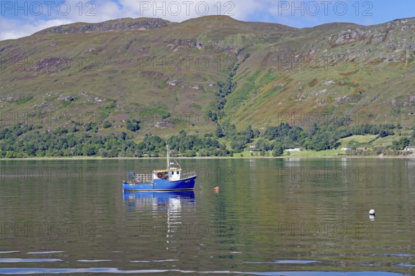 Small boat floating on a calm lake surrounded by green mountains, Fort William, Scotland, United